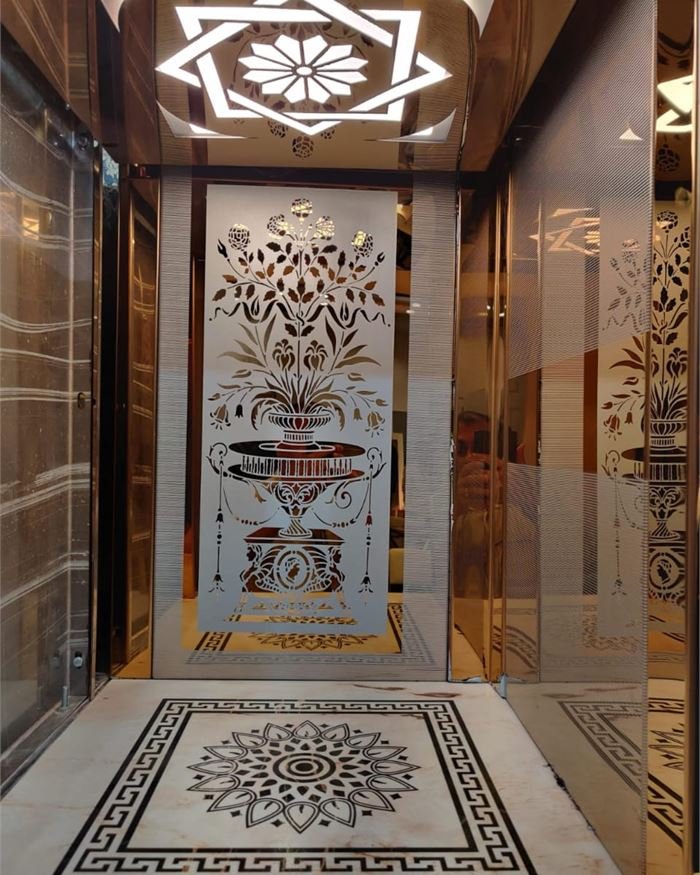 A lift cabin in gold mirror steel with etched floral panels and a marble inlay floor