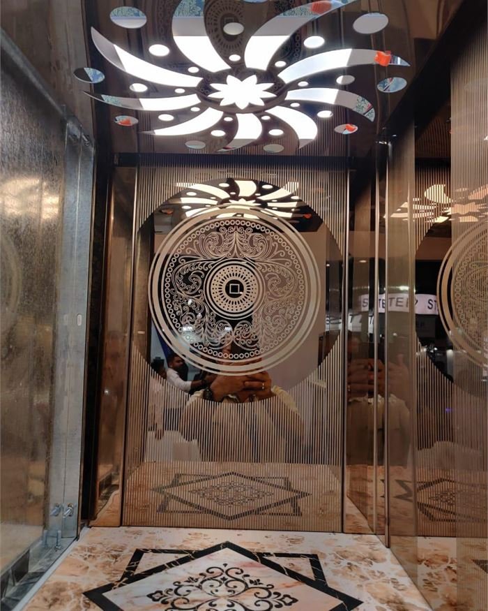A mirror-finish lift cabin with a cut-pattern ceiling and a stone medallion floor