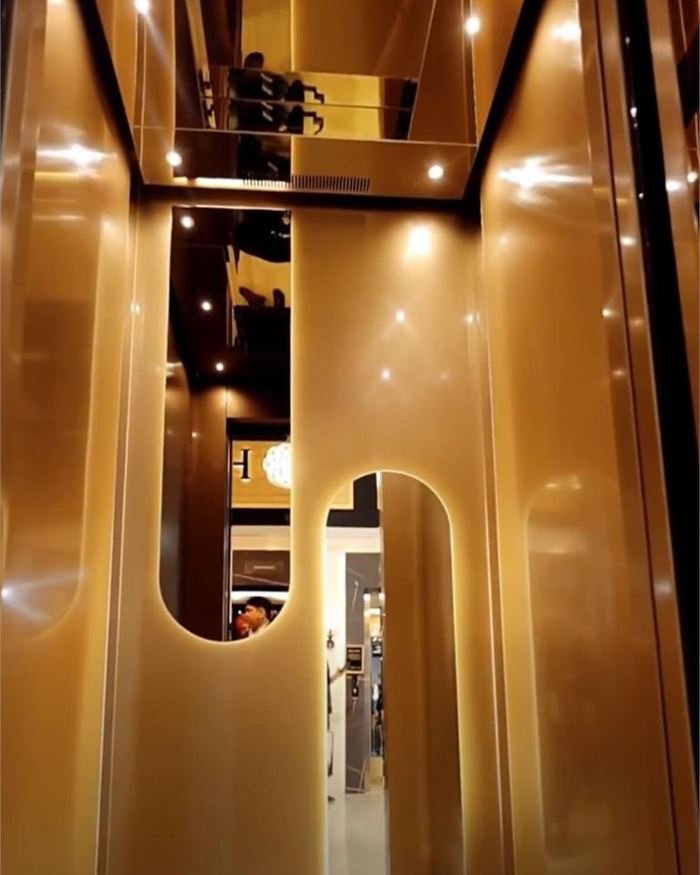 A champagne gold lift cabin with a curved feature wall and a lit ceiling