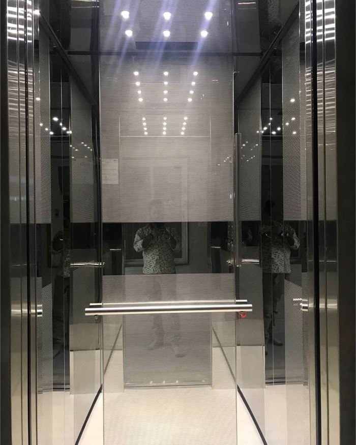 A grey mirror steel lift cabin with a full-height mirror and recessed ceiling spots