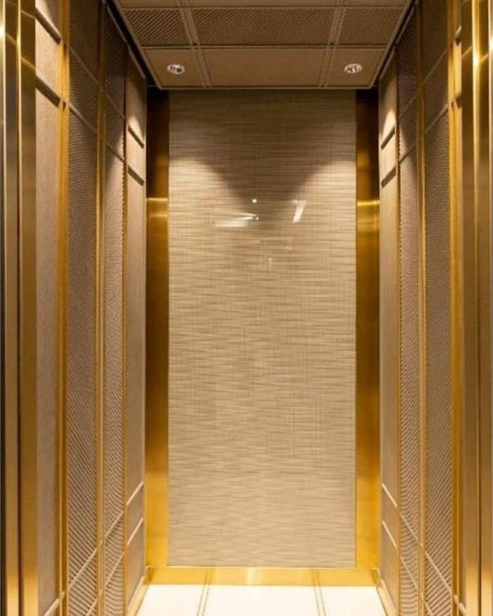A gold lift cabin with a fluted rear wall and a lit perimeter ceiling