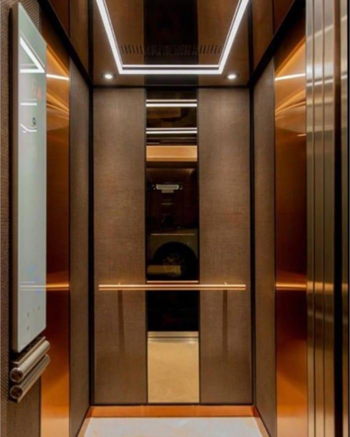 A bronze mirror lift cabin with a framed cove-lit ceiling and a wood centre panel