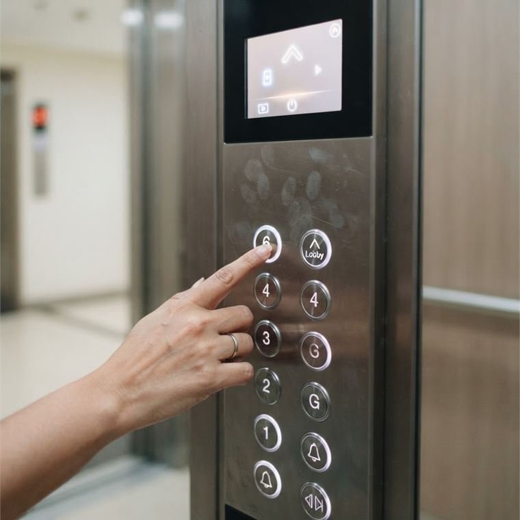 A hand pressing a floor button on a stainless car operating panel with a touch display above it