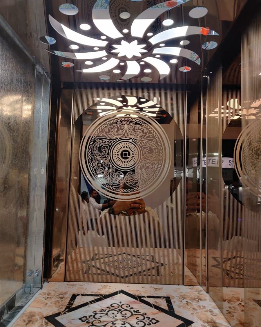 A mirror-finish lift cabin with a patterned ceiling and a marble inlay floor