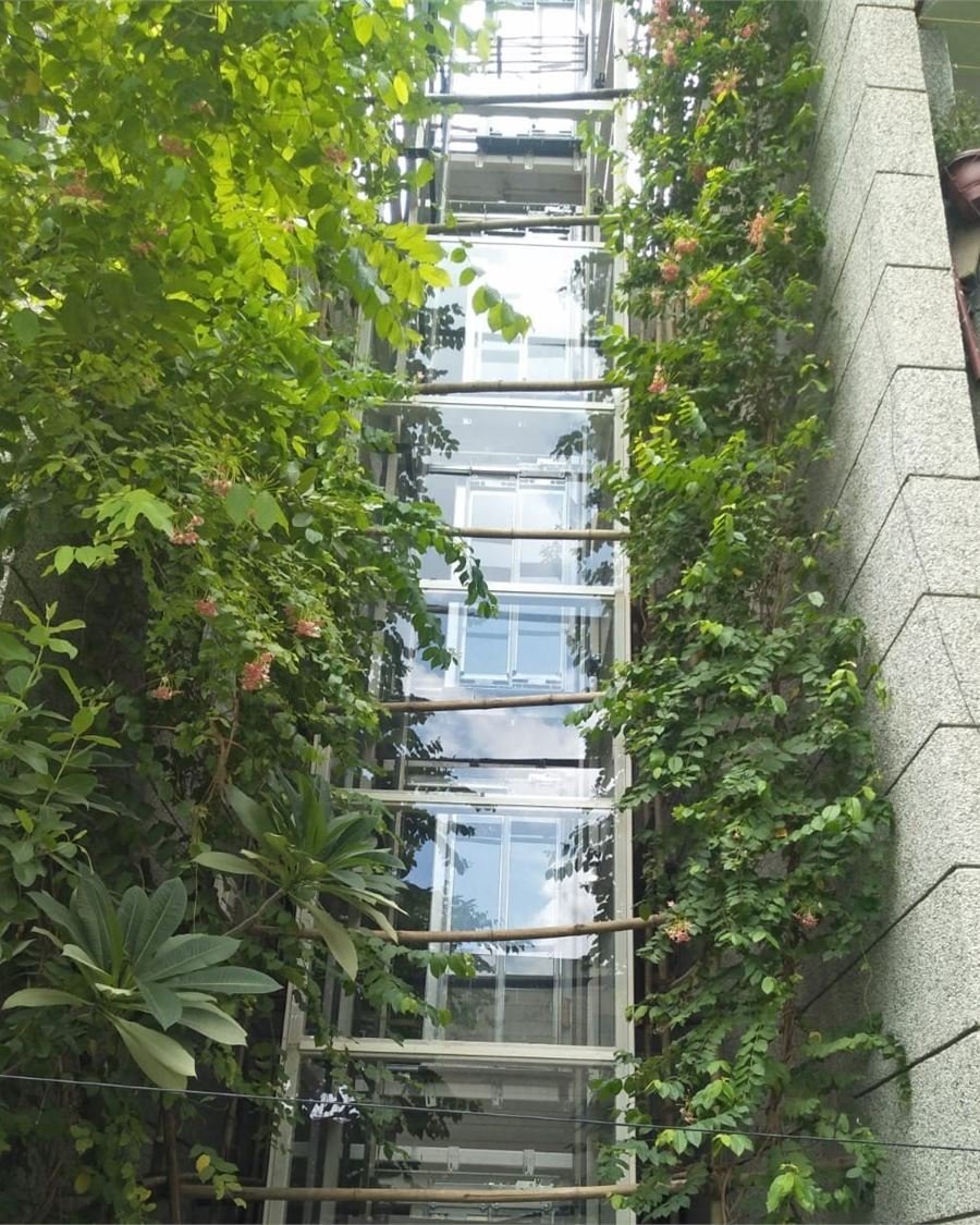 A glazed structure lift rising through a planted courtyard between two residential blocks